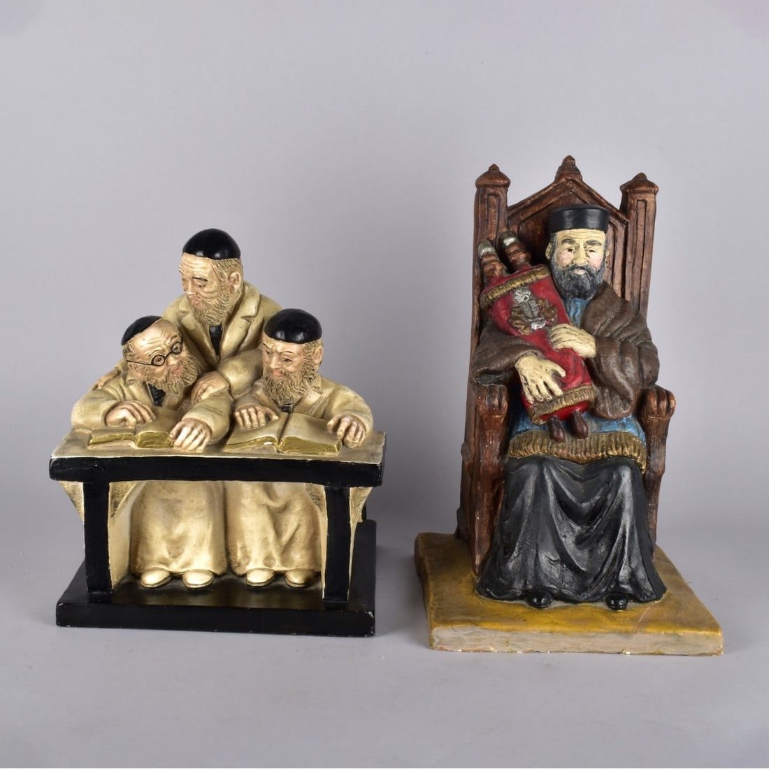 Two Judaica Figurines: Two Judaica Painted Plaster Figurines, Rabbi in chair measures13-3/4" H x 8-5/8" square. Rabbis reading 1measures 1-1/2" H x 9-5/8" W x 8-3/8". Condition: Front corner of Rabbi in chair is broken and
