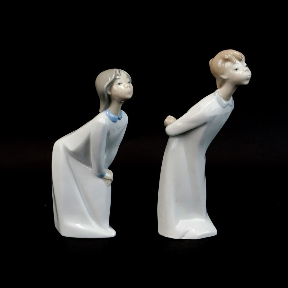 Two Lladro "Kissing" Figurines: Lot of Two Lladro "Boy and Girl Kissing" Glazed Porcelain Figurines. Signed. Boy measures 8" x 2-3/8" x 4". Girl measures 7-1/4" x 1-3/4" x 4". Condition: Good condition. Estimate: $50.00 - $150.00 Do