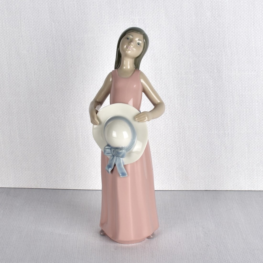 Lladro Porcelain Figurine: Lladro Porcelain Figurine "Dreamer Girl with Hat". Marked "Lladro Hand Made in Spain". 20th century. Measures: 9-1/2" H, 3-1/4" W, 3-1/4" D. Condition: Excellent condition. Estimate: $50.00 - $100.00 