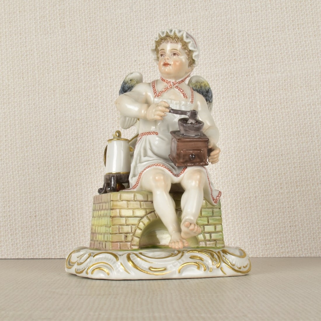 Meissen Figurine of a Young Boy Grinding Coffee: Meissen Porcelain Figurine of a Young Winged Boy Grinding His Coffee Sitting on a Fireplace with His Coffee Pot to the Side. Marked with the Meissen Crossed Swords Under Glaze as well as Incised Numbe
