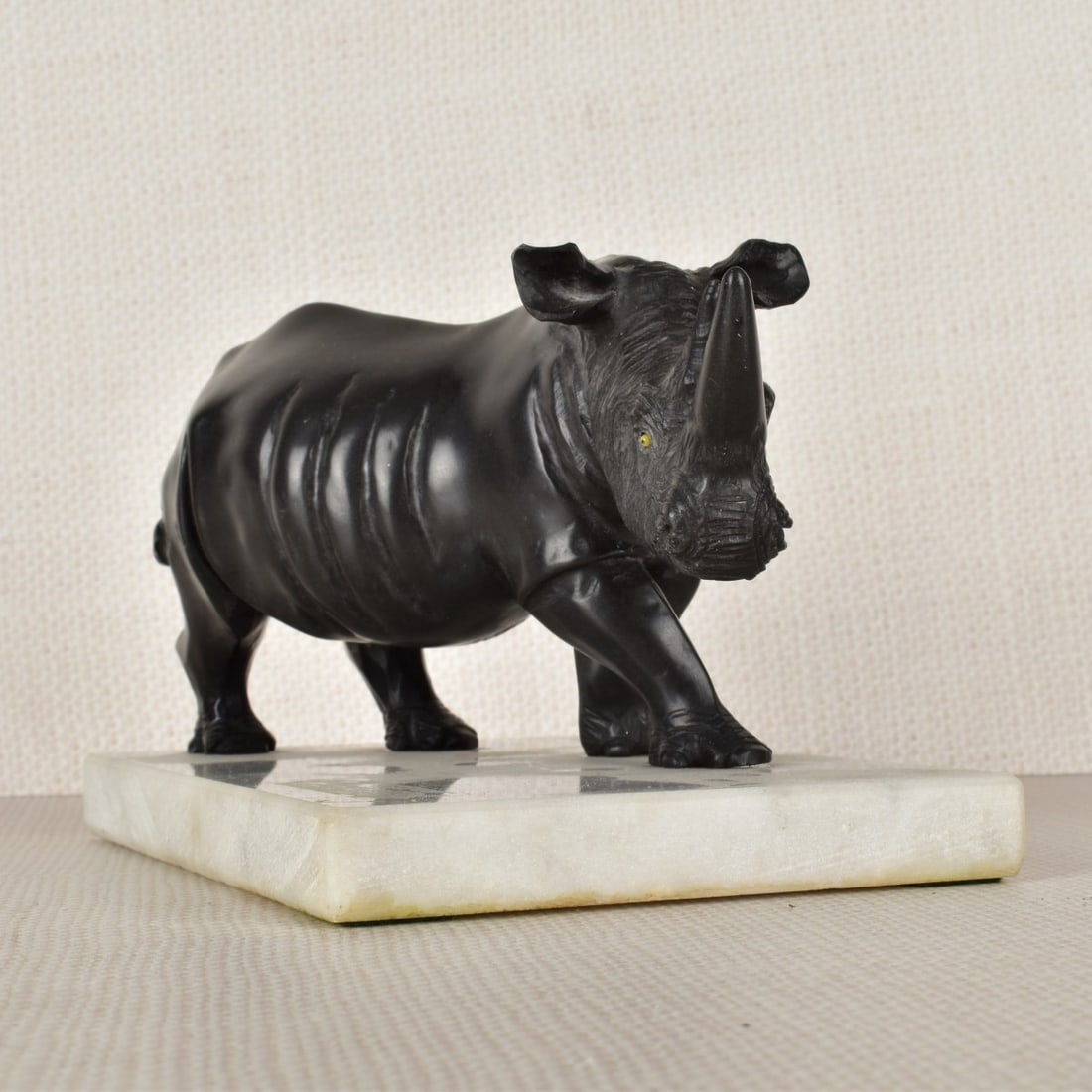 Carved Rhinoceros: Carved Wonderstone Figurine of a Rhinoceros Mounted on a White Veined Marble Base. Figure measures: 3" H, base measures: 1/2" H, 6-1/4" L, 4" D. Condition: Good condition, very small flea bite to ridg