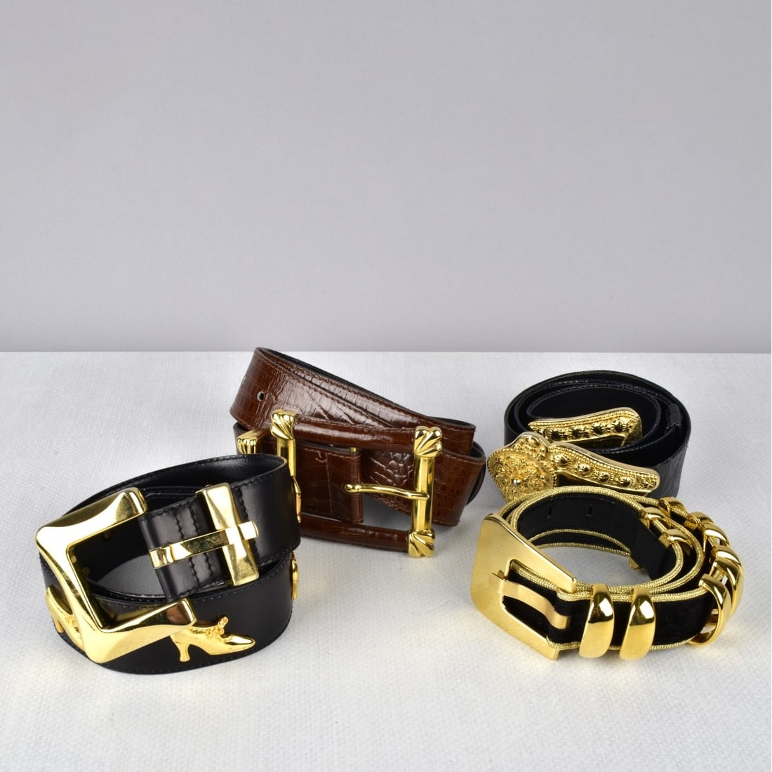 Four Designer Belts: Four Designer Belts some Escada, three in dust bags. a Black leather belt with goldtone buckle and shoe accent, marked size 38. a Black suede, gold edging with goldtone buckle and slide accent, marked