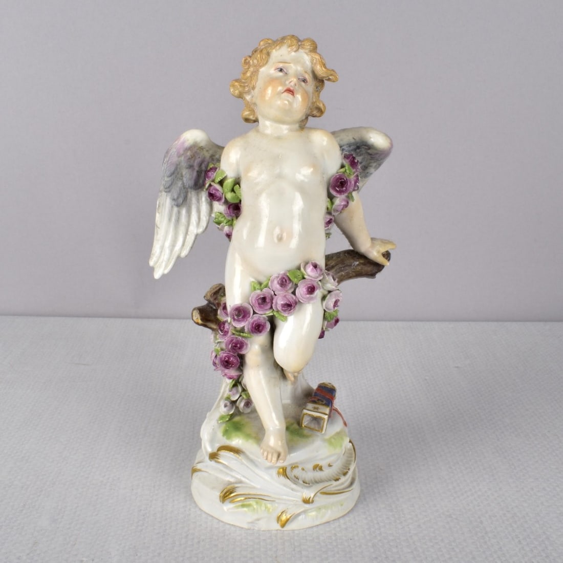 Meissen German Porcelain Figurine: Meissen German Porcelain Figurine of a Putti with a Sad Face, The winged child with a draped garland of roses. Properly marked with the Meissen signet under glaze. 19th century. Also incised "R123 and