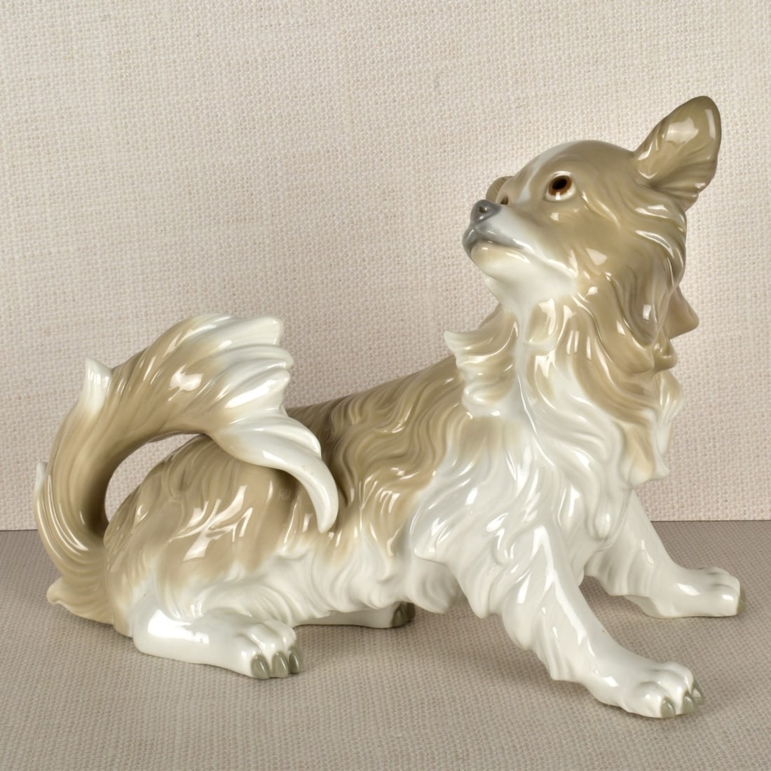 Lladro Figurine of a Papillion: Lladro Porcelain Figurine of a Papillion Looking Back and Up with its Tail Curled Over the Back. Properly marked on the bottom. Measures:8" H, 11" W, 5" D. Condition: Good condition. Estimate: $100.00