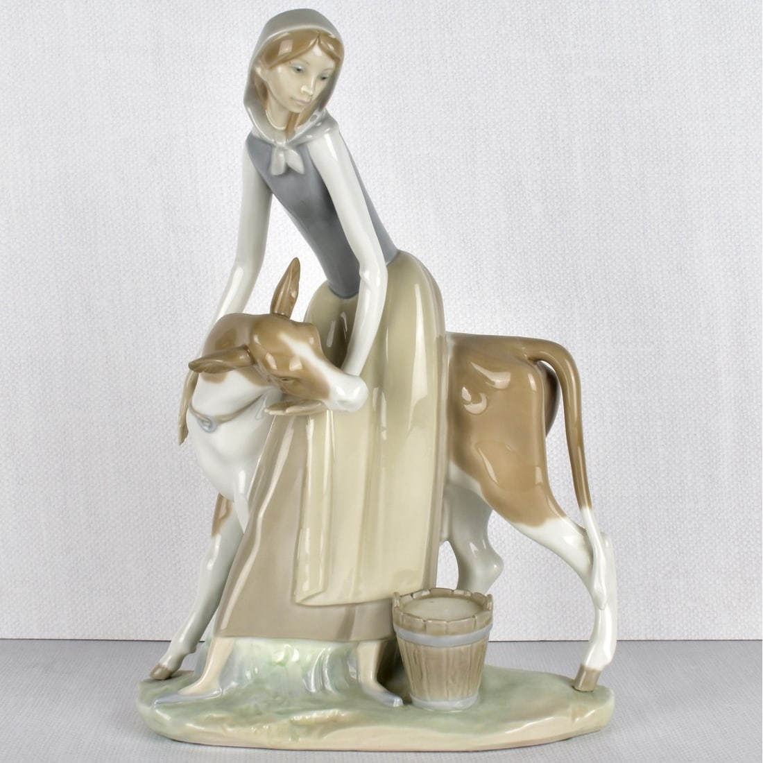 Lladro Porcelain Figurine of a Milkmaid: Lladro Porcelain Figurine of a Milkmaid Standing Next to a Cow and a Bucket of Milk to her Side. Properly marked to the bottom. Measures: 13-1/2" H, 10" W, 6-1/2" D. Kodner Galleries offers phone and