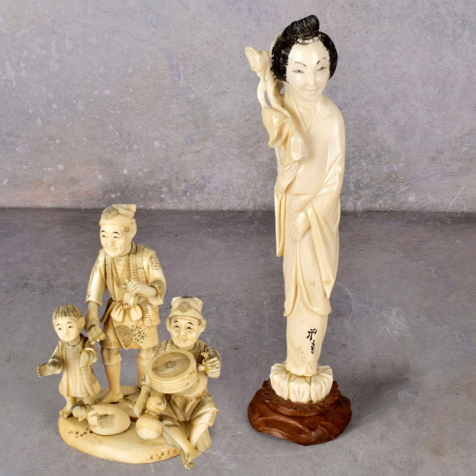 Vintage Japanese Carved Okimono Figures: Two (2) Vintage Japanese Carved Okimono Figures. One (1) lady standing with flowers, signed, mounted to a wood base, overall, with base measures: 9-1/2" H., one (1) man and children with drum, measure