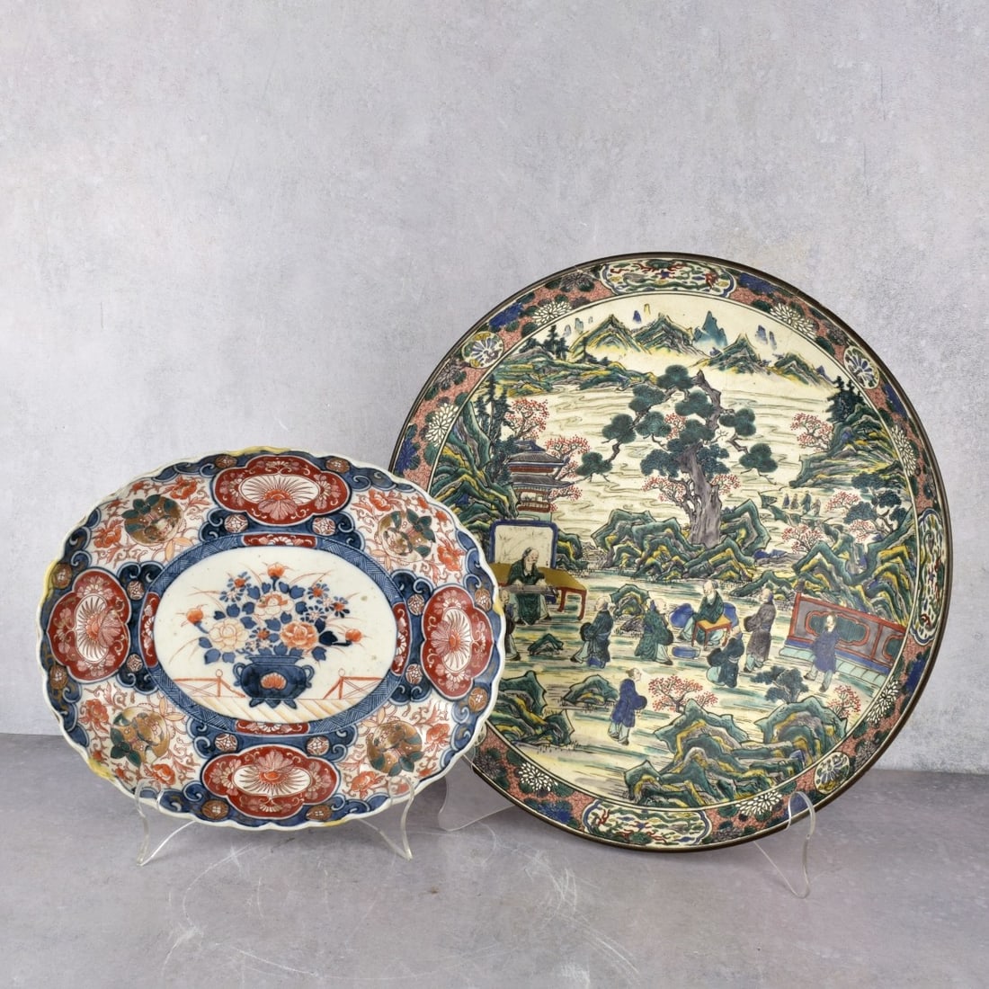 Antique Japanese Porcelain Plates: Two (2) Antique Japanese Porcelain Plates. One (1) Imari oval plate with scalloped edges, measures: 2" H., 11" W., 9" D., one (1) landscape plate, measures: 2-3/8" H., 14" Dia. Kodner Galleries offers