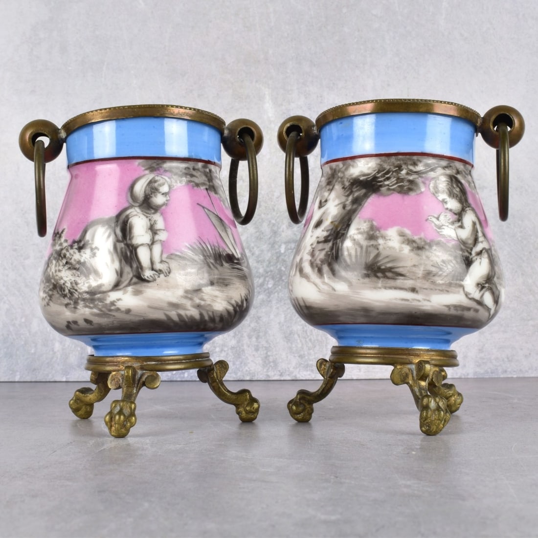 Antique Pair of Scenic Porcelain Pots: Antique Pair of Scenic Porcelain Pots with Brass Handles and Three (3) Footed Paw Feet Pots. Measures: 4-1/2" H., 3" D. Kodner Galleries offers phone and absentee bidding at a low, flat 21% buyer’s