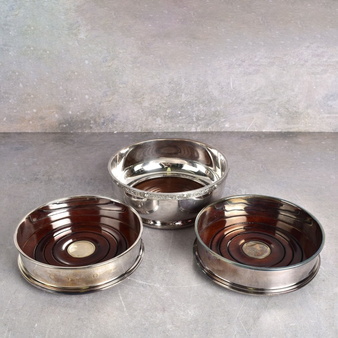 English 925 Sterling Silver Wine Coasters: Three (3) English 925 Sterling Silver Wine Coasters with Rosewood Bottoms. Two (2) by one maker, one (1) by another maker. Properly marked to the bottoms. Largest measures: 2-1/4" H., 5-1/2" Dia. All
