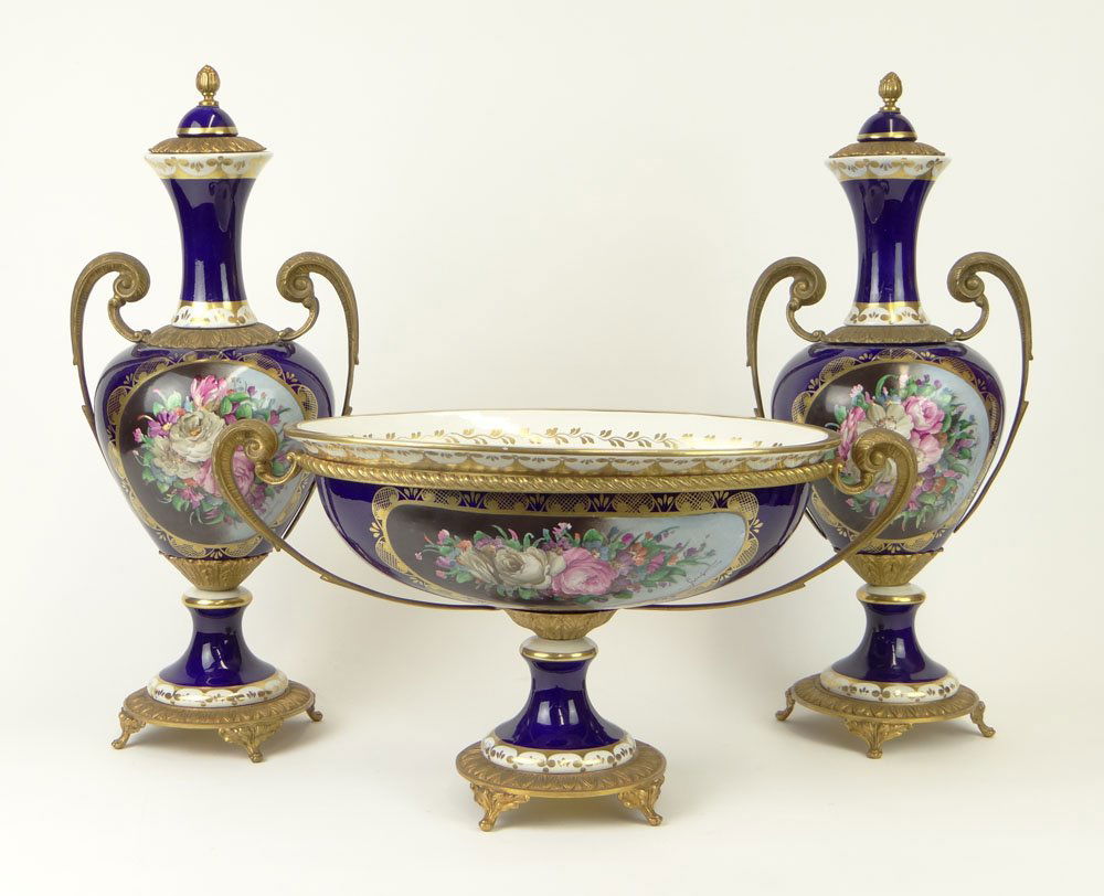 20th Century Three (3) Piece Sevres-style Gilt Bronze M: 20th Century Three (3) Piece Sevres-style Gilt Bronze Mounted Cobalt Porcelain Garniture Set with Painted Floral Reserves Comprising a Pair of Urns and a Footed Compote. Illegible Artist Signature to