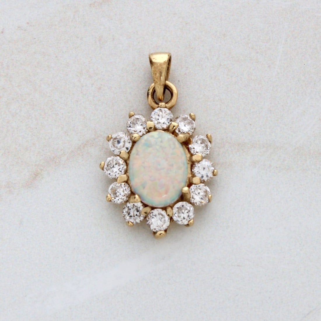 Opal, Sapphire and 14K Pendant: Vintage Opal and 14 Karat Yellow Gold Pendant with White Sapphire Bezel. Opal with good play of color. Stamped 14K. Measures 7/8" L, 5/8" W. Approx. weight: 2.95 grams. Kodner Galleries offers phone a