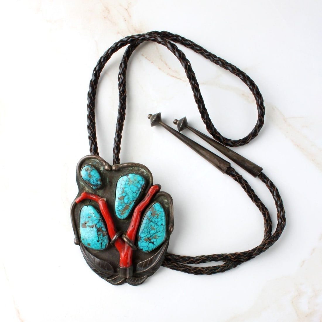Navajo Coral, Turquoise and Silver Bolo Tie: Vintage Navajo Red Coral, Turquoise, Silver and Braided Leather Bolo Tie. Signed (unidentified maker). Slider measures 3-1/2" H, 2-5/8" W; tie measures 40" L. Approx. gross weight: 96.55 grams. Condit