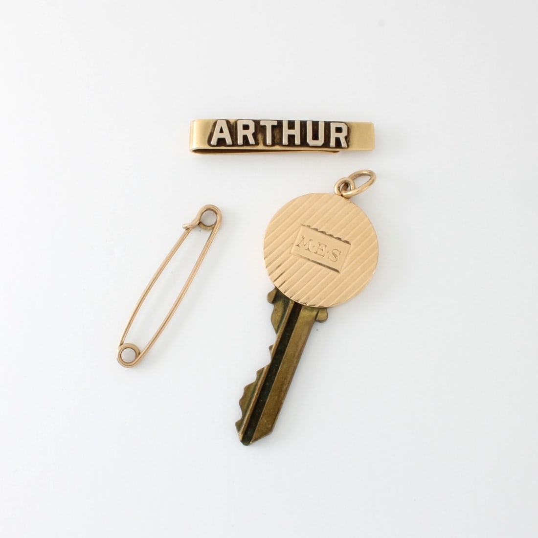 14K Gold: Vintage 14 Karat Yellow Gold. To include a tie bar with raised "Arthur" (5.54 grams), a safety pin (1.18 grams) and a door key top engraved 'MES" (gross weight: 10.59 grams). Tie bar measures 1-3/8" L