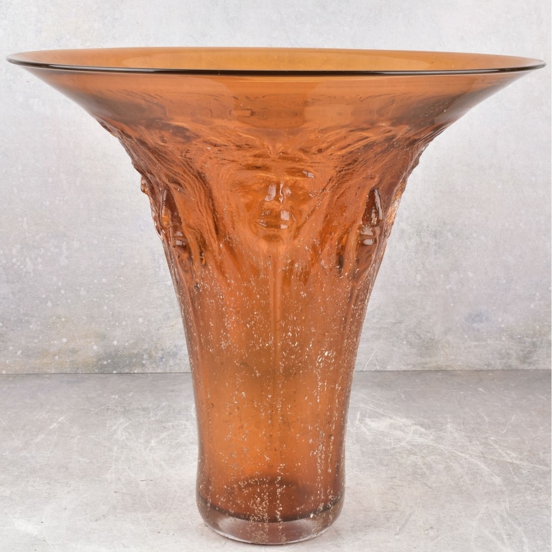 Art Glass Amber Glass Vase: Large Art Glass Amber Trumpet Shape Vase with Dimensional Mask Faces all Around and Designed with a Rough Surface. Engraved signature to the bottom. Measures: 14-1/4" high, top rim measures:15-1/2 dia