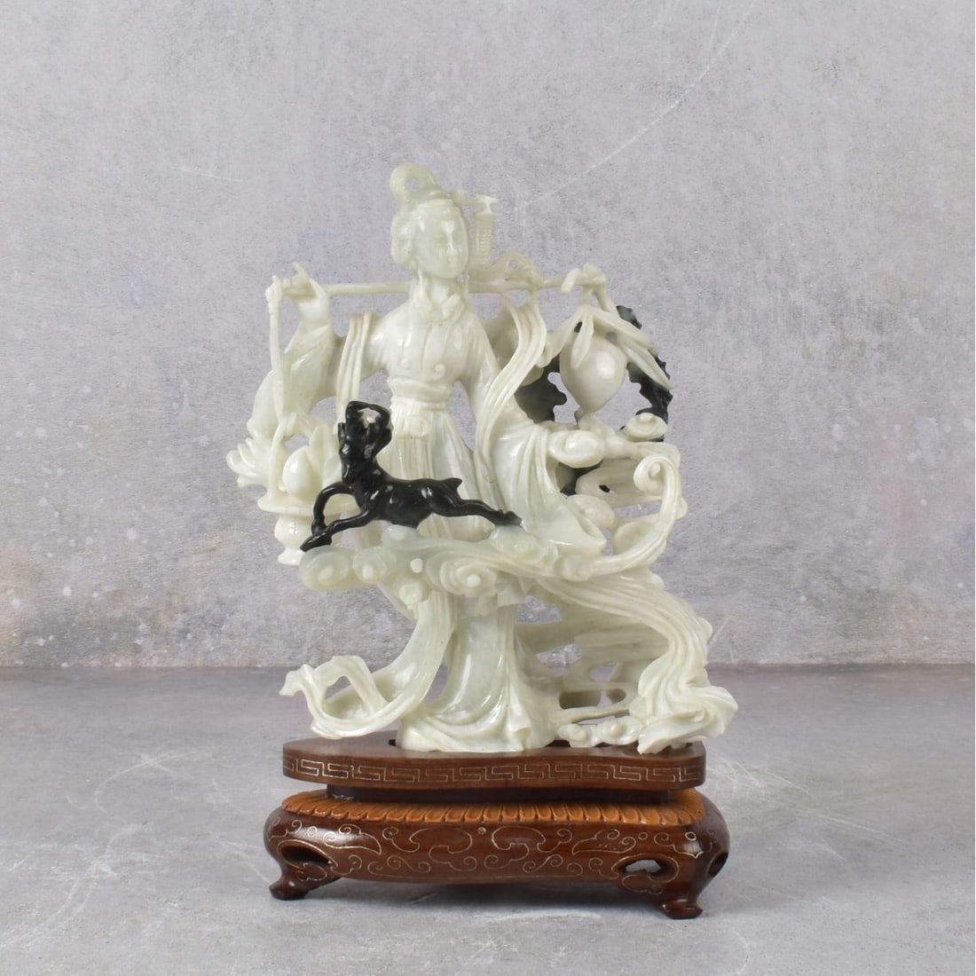 Chinese Carved Jade Guanyin on Wooden Base.: Chinese Carved Jade Guanyin with a Small Deer on a Carved Wooden Base. Circa 1970. Figure measures: 6" H, 5-1/2" W, 3-1/2" D. Kodner Galleries offers phone and absentee bidding at a low, flat 21% buye