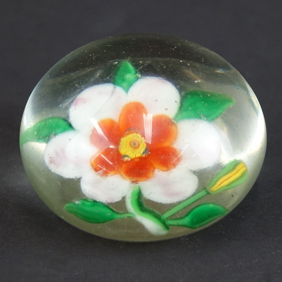 Antique Baccarat Paperweight: Antique Baccarat Clematis Art Glass Paperweight. Designed with single clematis flower en center with green, orange, white and pink petals. L.H. Selman auction label attached. Measures 2" H x 2-3/4" W.