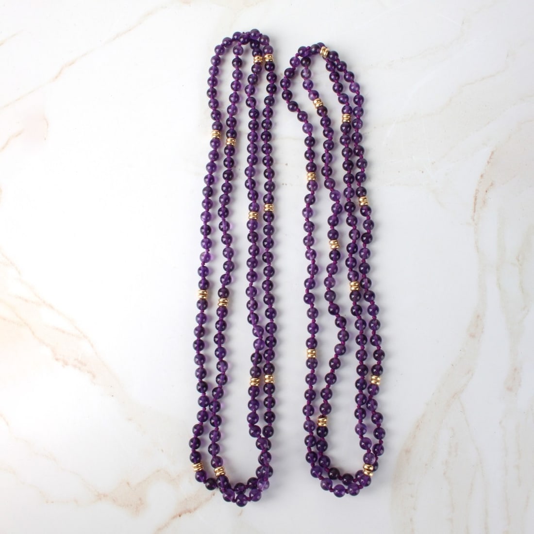 Amethyst and 14K Necklaces: Two Vintage Single Strand 5mm Amethyst Bead Necklaces with 14 Karat Yellow Gold Spacers. Measure 32" L and 34" L. Approx. total weight: 49.11 grams. Kodner Galleries offers phone and absentee bidding