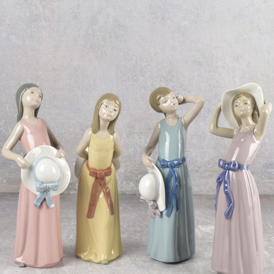 Lladro "Girl with Hat" Sculptures: Four (4) Lladro "Girl with Hat" Gloss Porcelain Sculptures. Each properly marked on bottom. Tallest measures: 10" high, 2 1/2" wide, 3-1/4" deep. Kodner Galleries offers phone and absentee bidding at