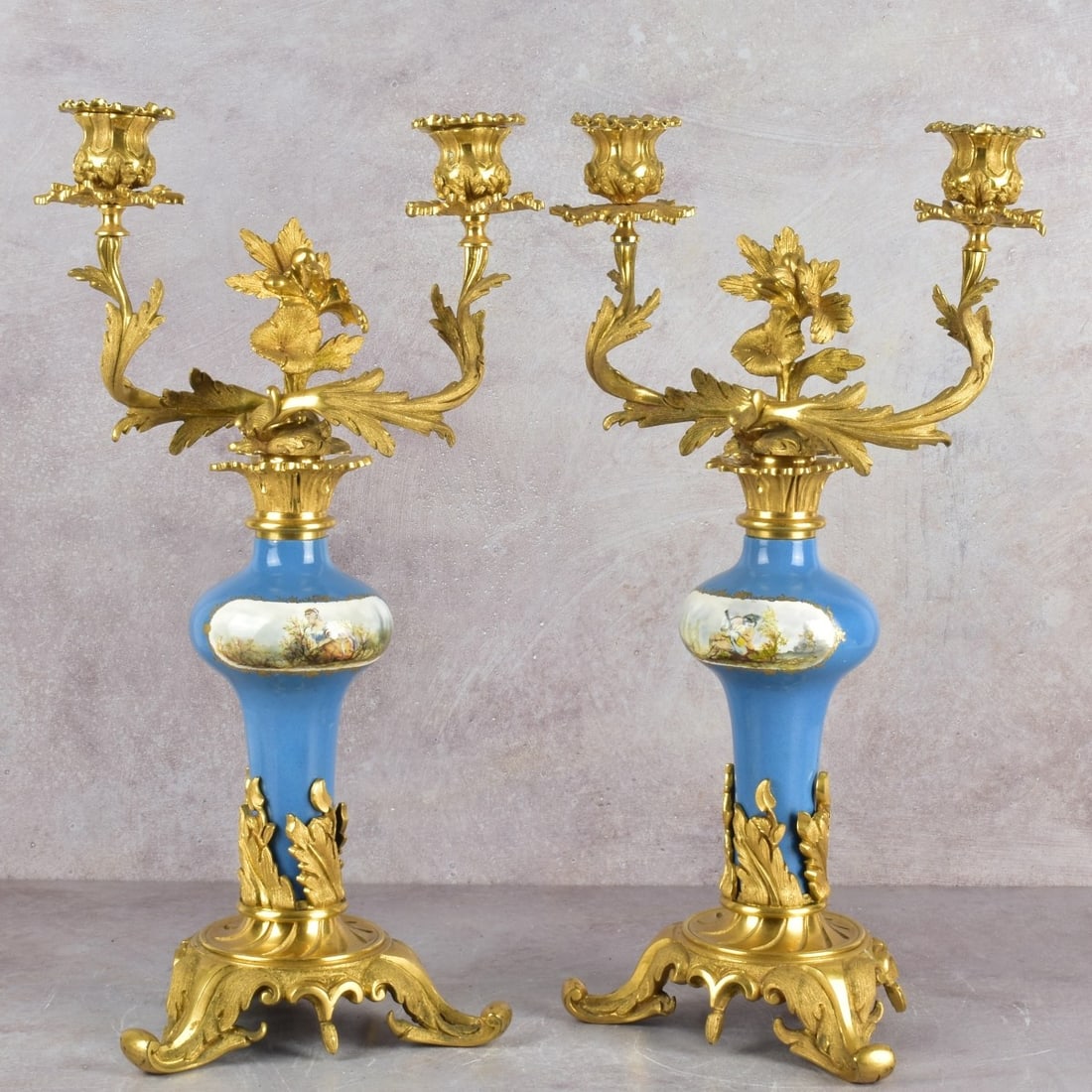 Sevres Style Candelabra: Sevres French Style Porcelain and Gilt Bronze Two (2) Light Candelabra with Hand Painted Romantic Scenes. 19/20th century. Measures: 18" high, 10" wide, 6-1/2" deep. Kodner Galleries offers phone and