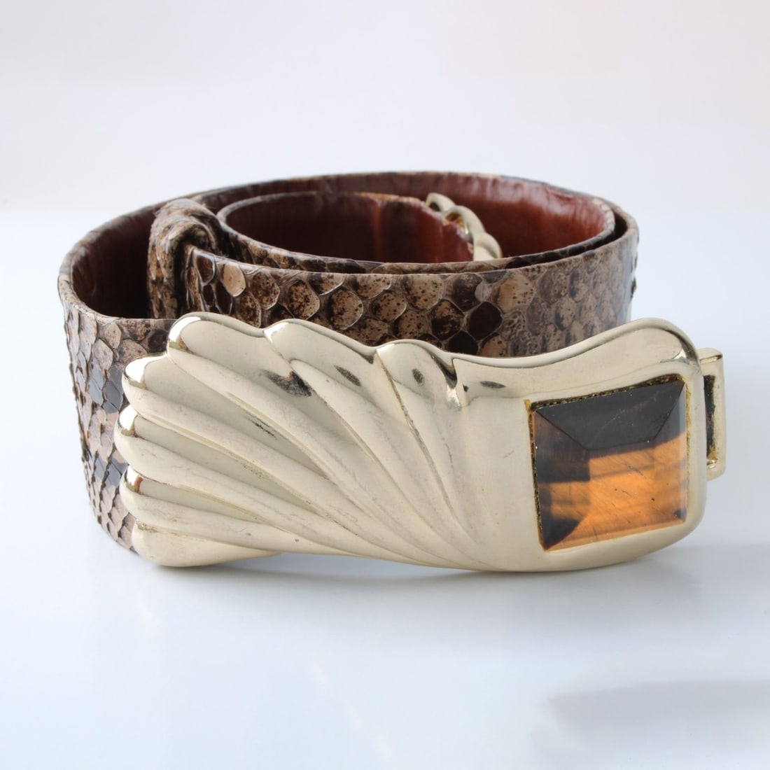 Judith Leiber Belt: Vintage Judith Leiber Snakeskin Belt with Tiger Eye and Gold Tone Metal Buckle. Signed. Measures 36" L, 1-3/4" W. With dust bag. Condition: Very good gentle used condition. Estimate: $50.00 - $150.00