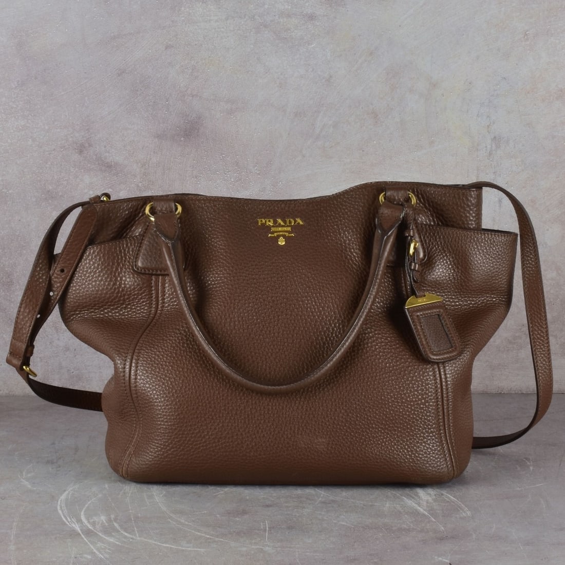 Prada Tote Bag: Vintage Prada Brown Leather Tote Bag with Gold Tone Hardware. Measures 11" H, 11-1/2" W, 6" D, 6-1/2" handle drop, Adjustable length shoulder strap. With luggage tag. No box. Kodner Galleries offers