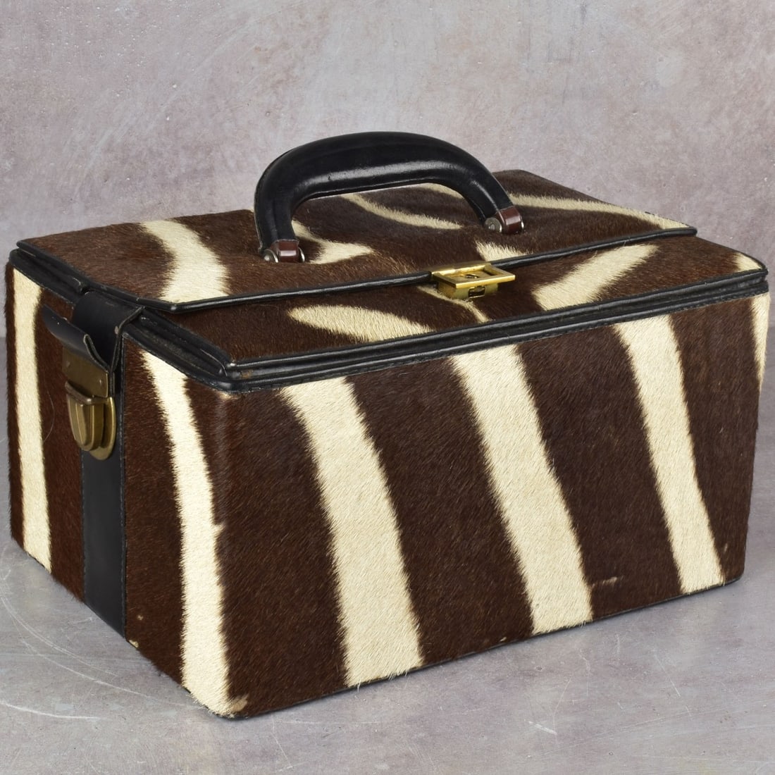 Zebra Skin Travel Case: Vintage Zebra Skin and Black Leather Travel Case with Brass Hardware. Suede fabric lining. Measures (closed) 6-1/2" H, 12" L, 8-1/4" D. Kodner Galleries offers phone and absentee bidding at a low,