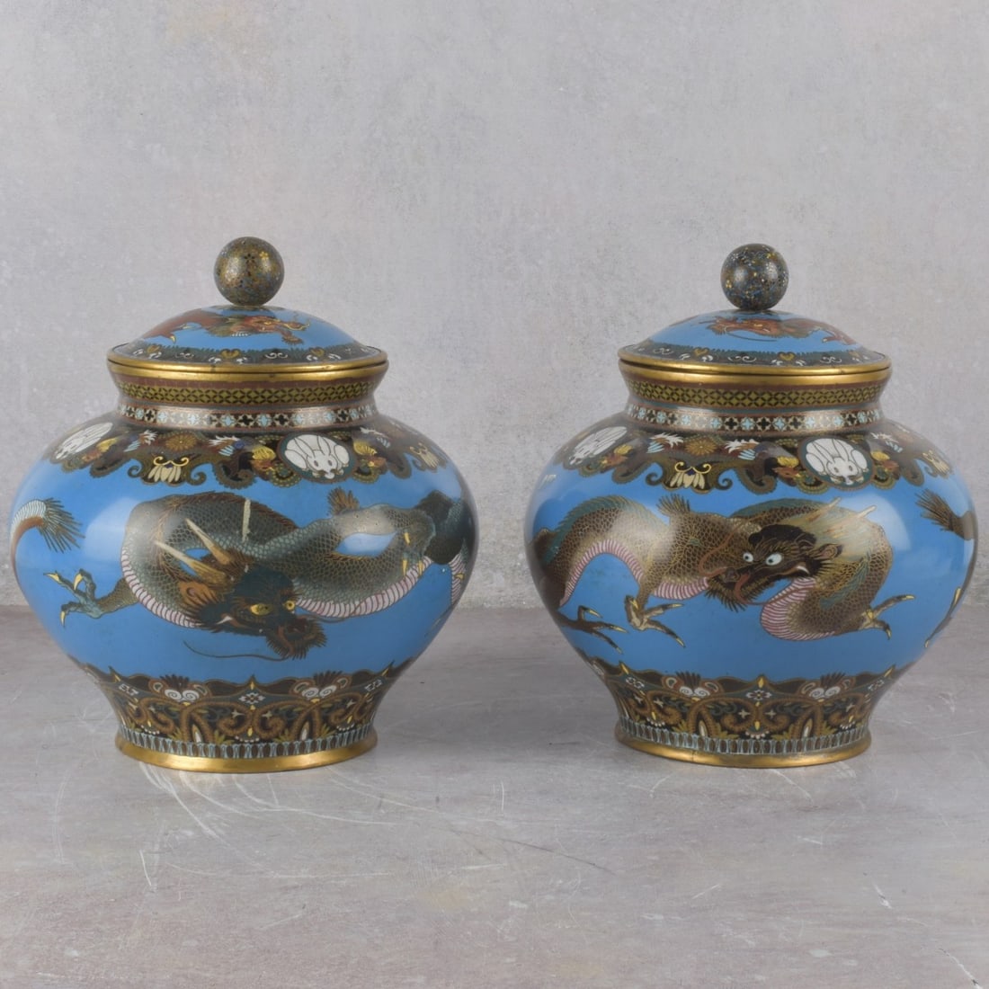 Japanese Cloisoinne Ginger Jars: Pair of Japanese Cloisoinne Ginger Jars on Copper. Late 19th century. Decorated with dragons, hares and a multitude of flowers finishing with a ball finial top on a blue ground. Measures: 10" high,