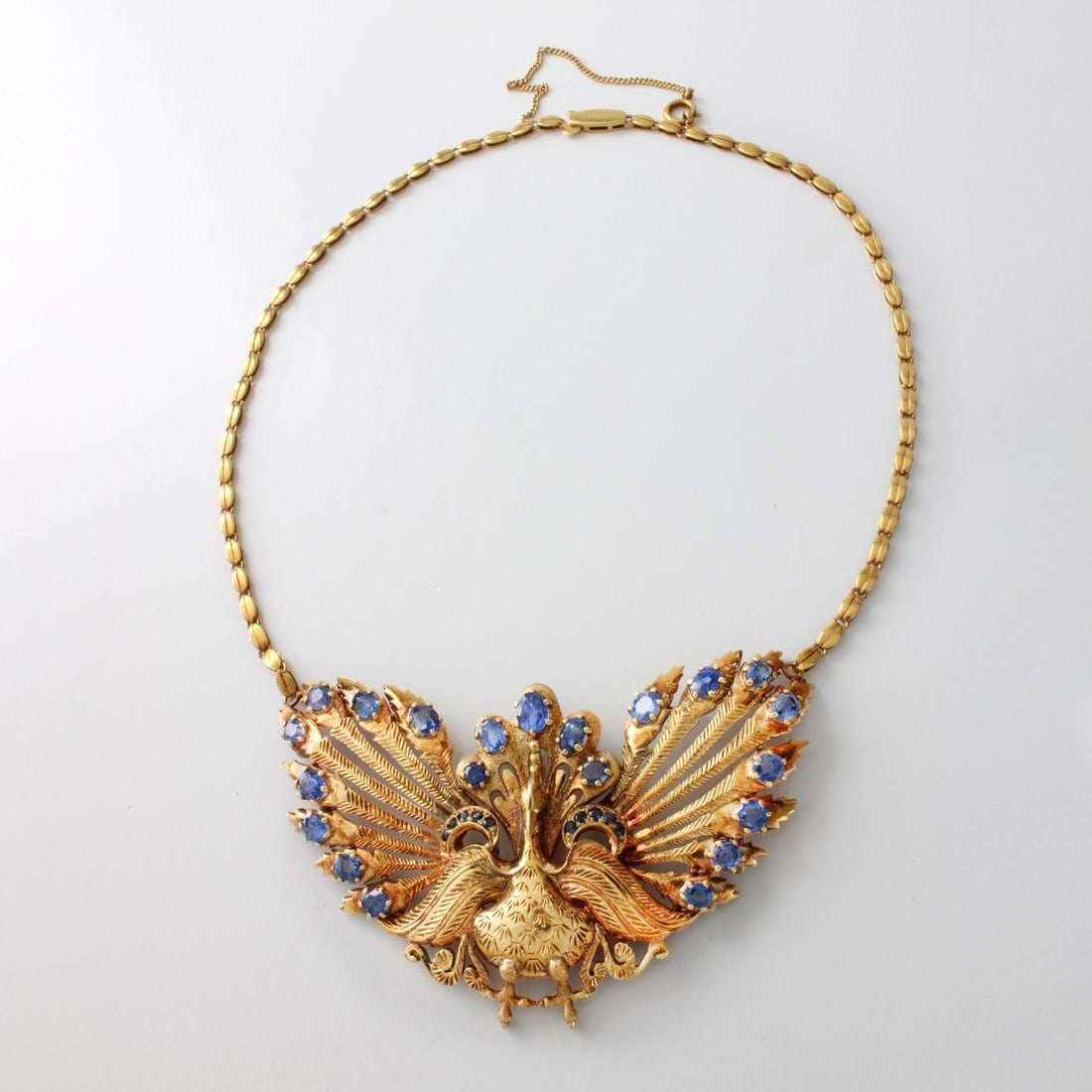 Sapphire and 18K Necklace: Vintage Approx. 8.0 Carat TW Oval and Round Cut Ceylon Sapphire and 18 Karat Yellow Gold Peacock Pendant Necklace. Sapphires with vivid color. Clasp stamped 18K. Pendant measures 2" H, 3-1/8" W;