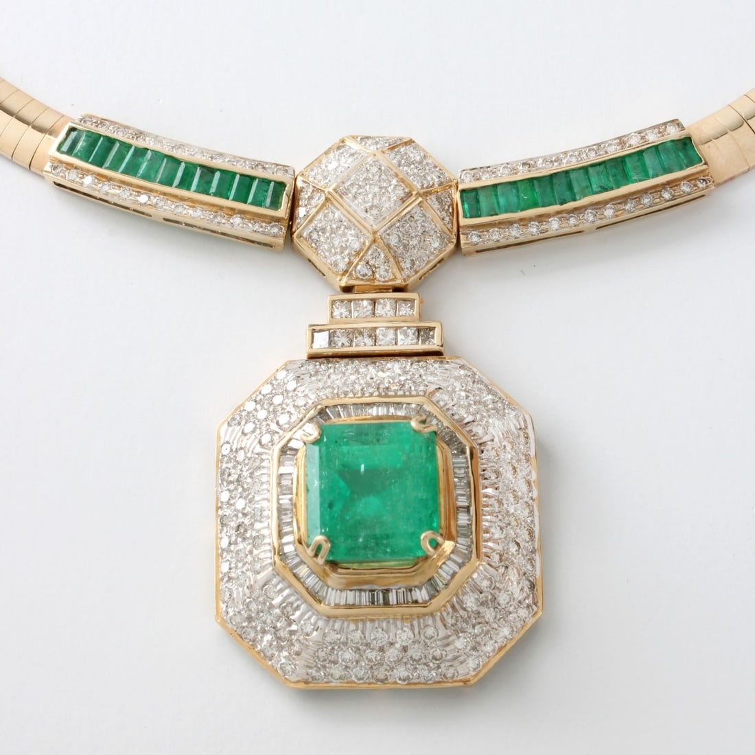 Emerald, Diamond and 14K Necklace: Vintage Emerald, Diamond and 14 Karat Yellow and White Gold Pendant Omega Necklace. Set in the center with an approx. 12.5 carat octagonal step cut Colombian emerald and accented with approx. 5.50