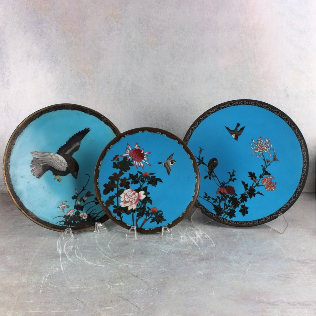 Japanese Bronze and Cloisonne Plates: Three (3) Japanese Meiji Period (1868-1912) Bronze and Cloisonne Display Plates Each Decorated with Small Birds in Flight and Flowers, the Reverse and Base in Bright Blue with Curled Wires. Largest