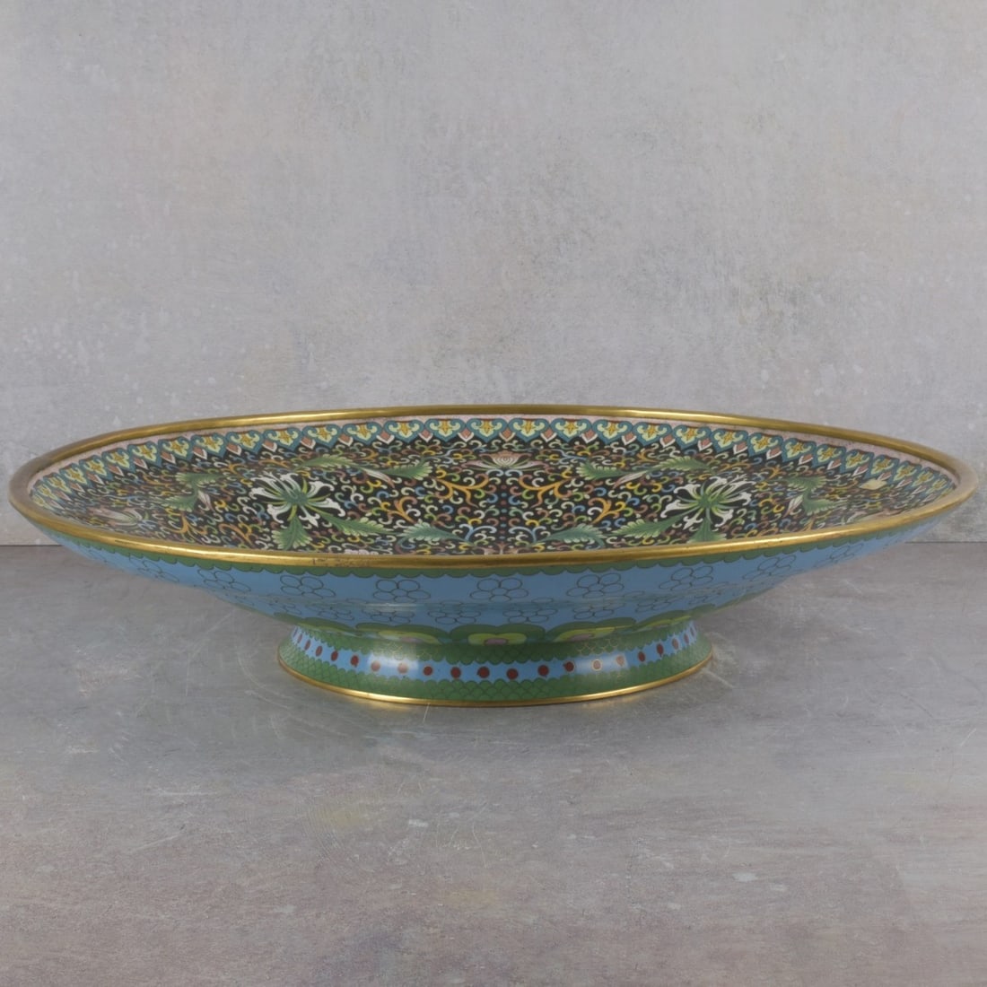 Large Cloisonne Platter: Large Cloisonne Center Piece Platter Decorated with Flowers and Scrolls. Measures: 3-3/4" high, 18" diameter. Kodner Galleries offers phone and absentee bidding at a low, flat 21% buyer’s premium