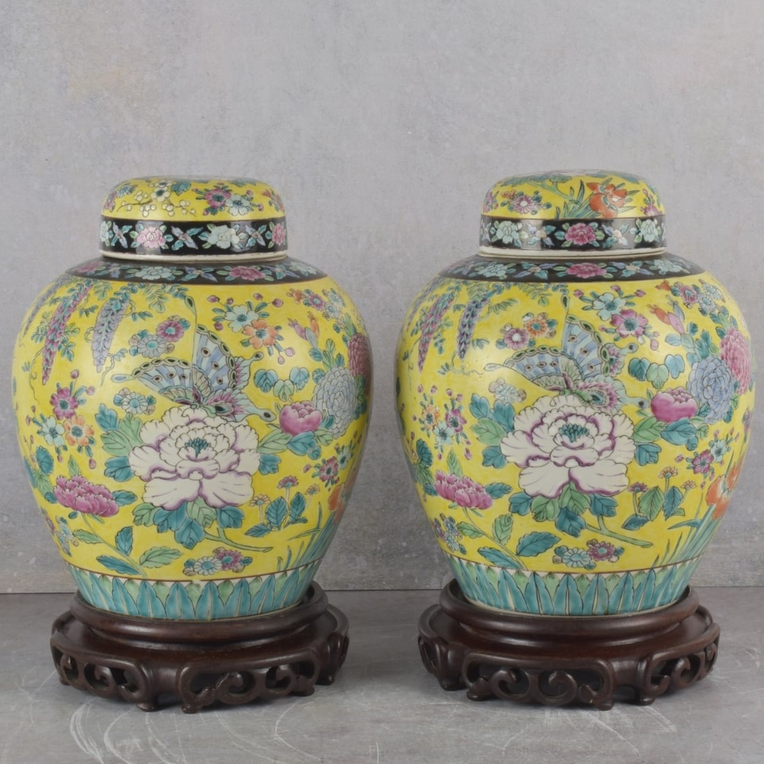 Pair of Chinese Ginger Jars: Vintage Pair of Chinese Famille Yellow Porcelain Ginger Jars Decorated with Large Flowers and Butterflies with Carved Wood Bases. Jars measure: 11-1/2" high, 8" diameter, bases measures: 2" high.