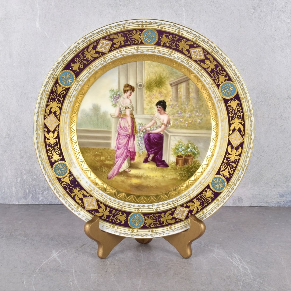 19/20th Century Royal Vienna Hand-Painted Cabinet: 19/20th Century Royal Vienna Hand-Painted and Gilt Porcelain Cabinet Plate Depicting Two (2) Female Figures in a Garden Conversing, Surrounded by a Raised Gilt Border. Blue beehive under glaze mark to