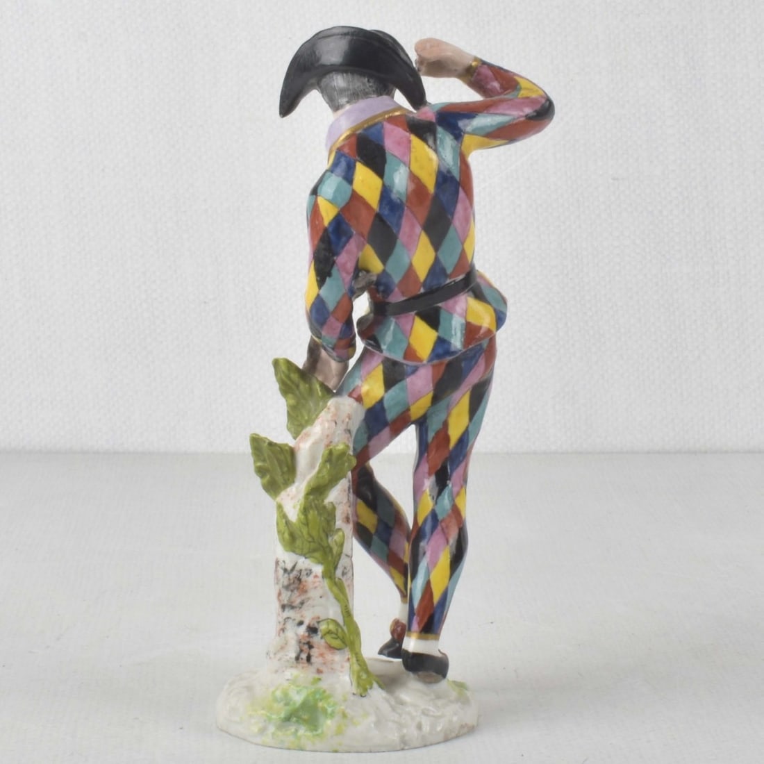 19th Century Figurine of a Masked Harlequin: 19th Century Porcelain Figurine of a Masked Harlequin Figure Standing Next to a Tree Stump. Marked France with a Pseudo Meissen Crossed Swords. Figure measures: 7-3/4" high, 3" wide, 2-1/8" deep.