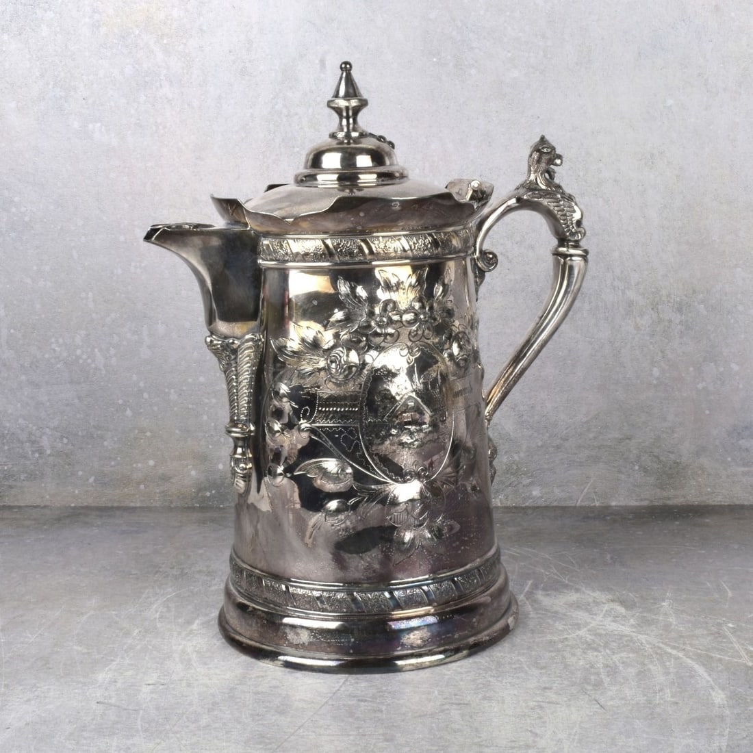Holmes and Son Baltimore Pitcher: Large 19th Century Silver Plate Insulated Pitcher. Deep repousse with a floral decoration to one side and a small house to the other side. Properly marked to the bottom. Measures: 13-1/2" high, 10-1/2