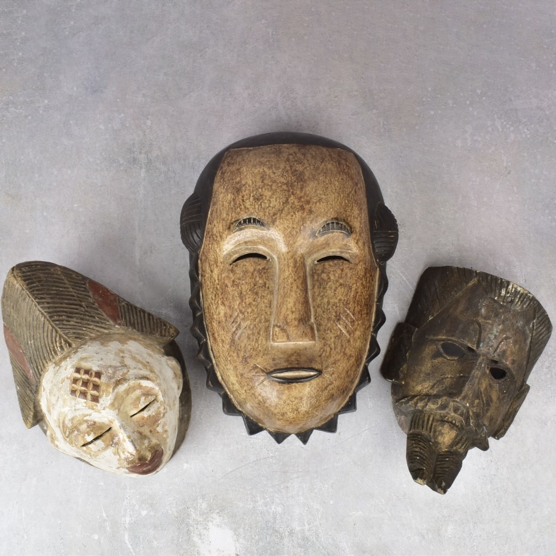 African Carved Wood Masks: Three (3) African Carved Wood Masks. Largest measures: 13" H., 9" W., 6-1/4" D., smallest measures: 9-1/8" H., 6-3/4" W., 3-3/4" D. Kodner Galleries offers phone and absentee bidding at a low, flat 21
