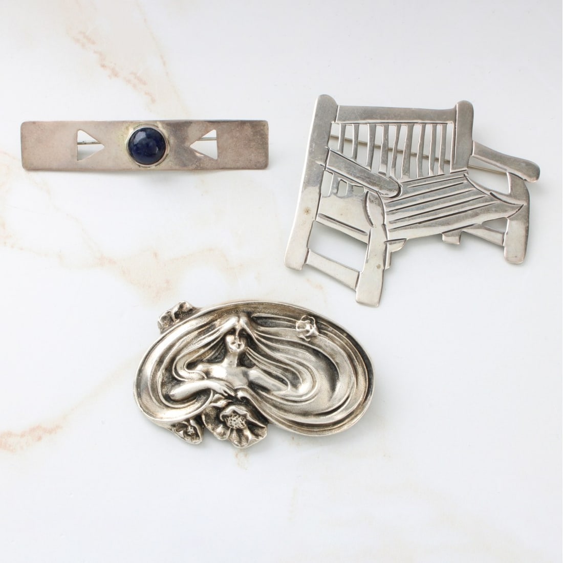 Silver Pins: Three Vintage Silver Pins. To include a figural bench, a bar pin with black onyx and a Metropolitan Museum of Art Art Nouveau style Lady. Bench stamped Sterling. Bench measures 2-1/4" H, 2-1/2" W.