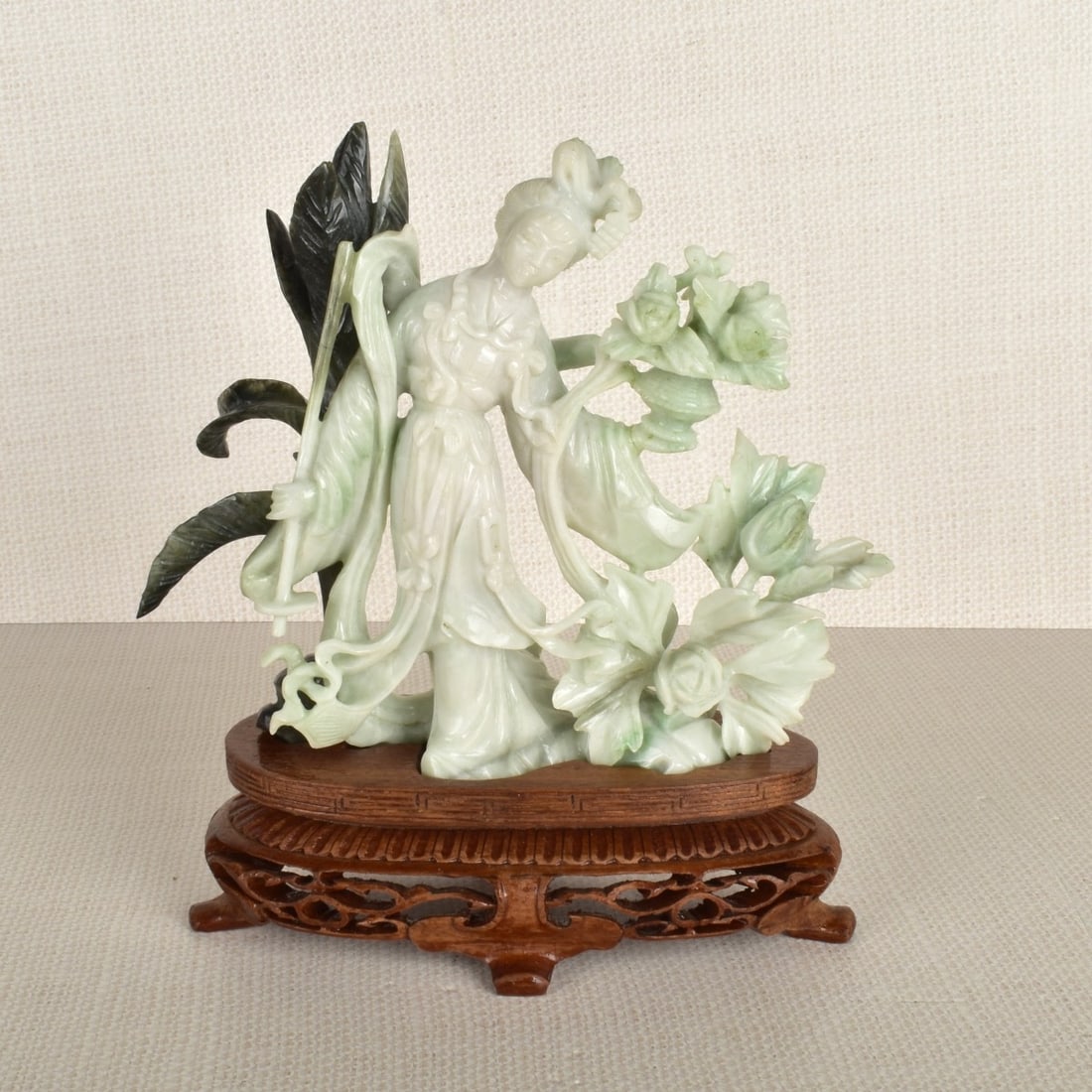 Chinese White Jade Figure: Carved Chinese White to Celadon Jade Figure of a Standing Lady Surrounded by Large Flowers and Leaves, Mounted on on a Carved Wood Fitted Base. 20th century. Figure measures: 5-1/2" H, 6-1/4" W, 1-1/2