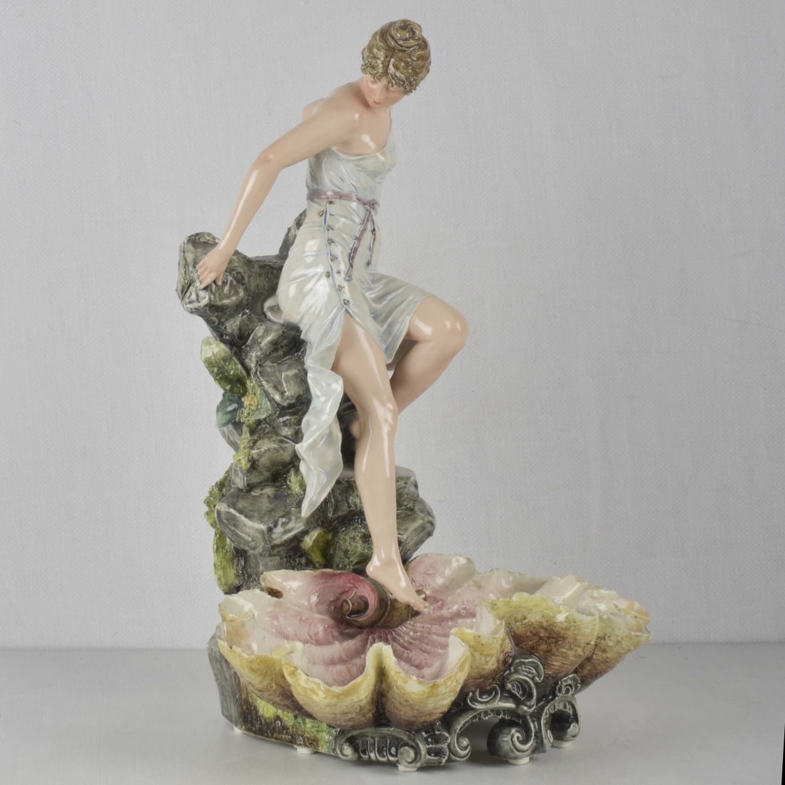 German Porcelain Sculpture: Early 20th Century German Art Nouveau Porcelain Sculpture of a Porcelain Sculpture of a Woman Testing the Waters Dipping Her Foot in a Shell Pond. Impressed marks to the bottom. Measures: 19" high,