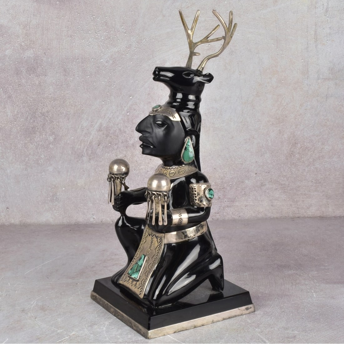 Obsidian and Sterling Silver Sculpture: Aztec Style Obsidian and Sterling Silver Sculpture with Malachite Insets. Mexico 20th century. Depicting a crouching figure wearing an animal headdress with antlers, holding ceremonial rattles,