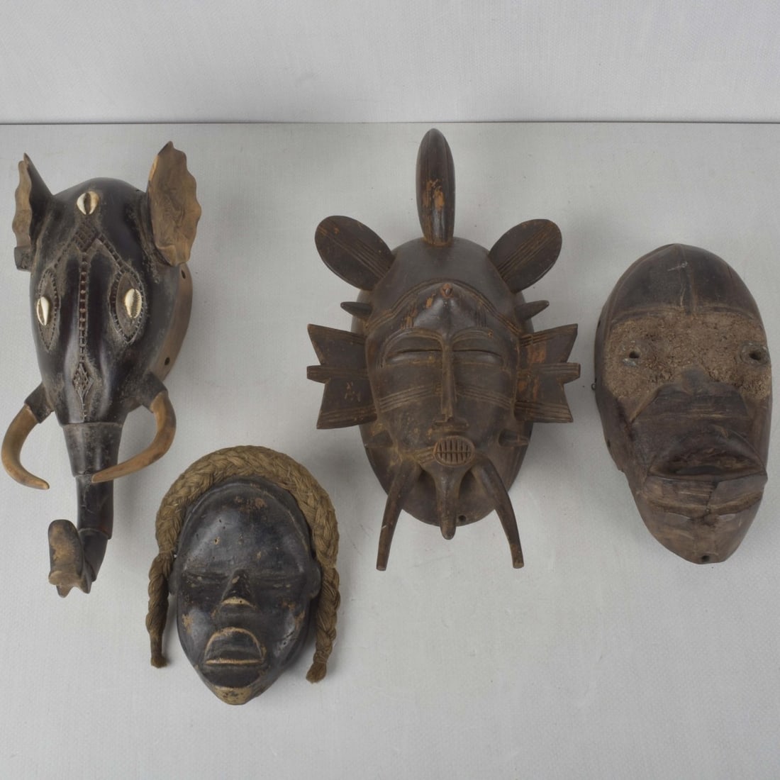 Vintage African Tribal Art Wood Sculptures: Four (4) Vintage African Tribal Art Wood Sculptures. One mask with attached cowie shells. Tallest measures: 15" high, shortest measures: 7" high. Kodner Galleries offers phone and absentee bidding at