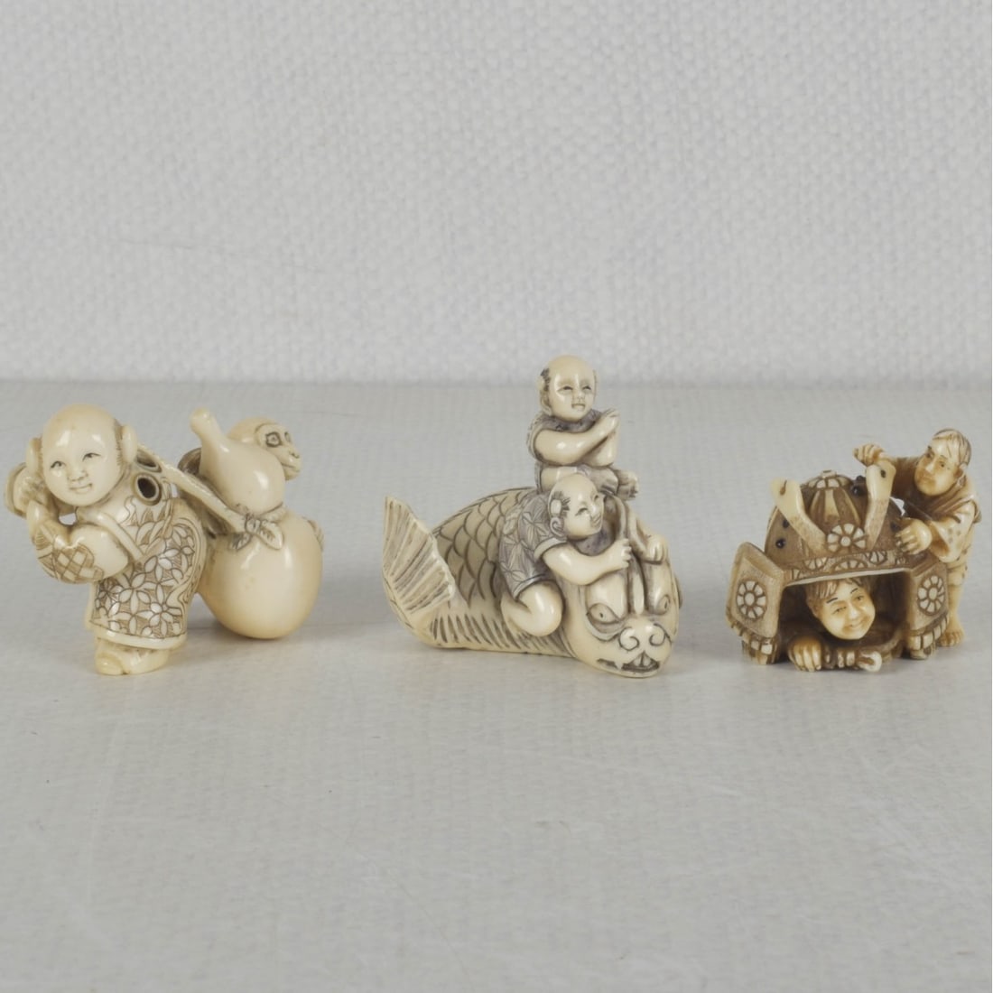 Japanese Netsukes: Three 20th Century Japanese Carved Netsukes. To include a boy on a fish, a boy with a gourd and a monkey, and two boys with a samurai helmet. Each signed. Boy on a fish measures 1-1/2" H, 1-5/8" W.