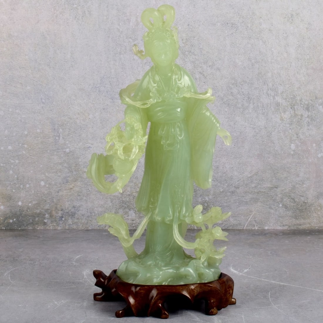 Chinese Carved Green Jade Guanyin Figure: Chinese Carved Green Jade Figure of a Guanyin with a Basket of Flowers. Mounted on a fitted wood base. Figure measures: 10-3/4" High, 5-1/2" Wide, 4" Deep. Base measures: 1-1/4" High. Kodner Galleries