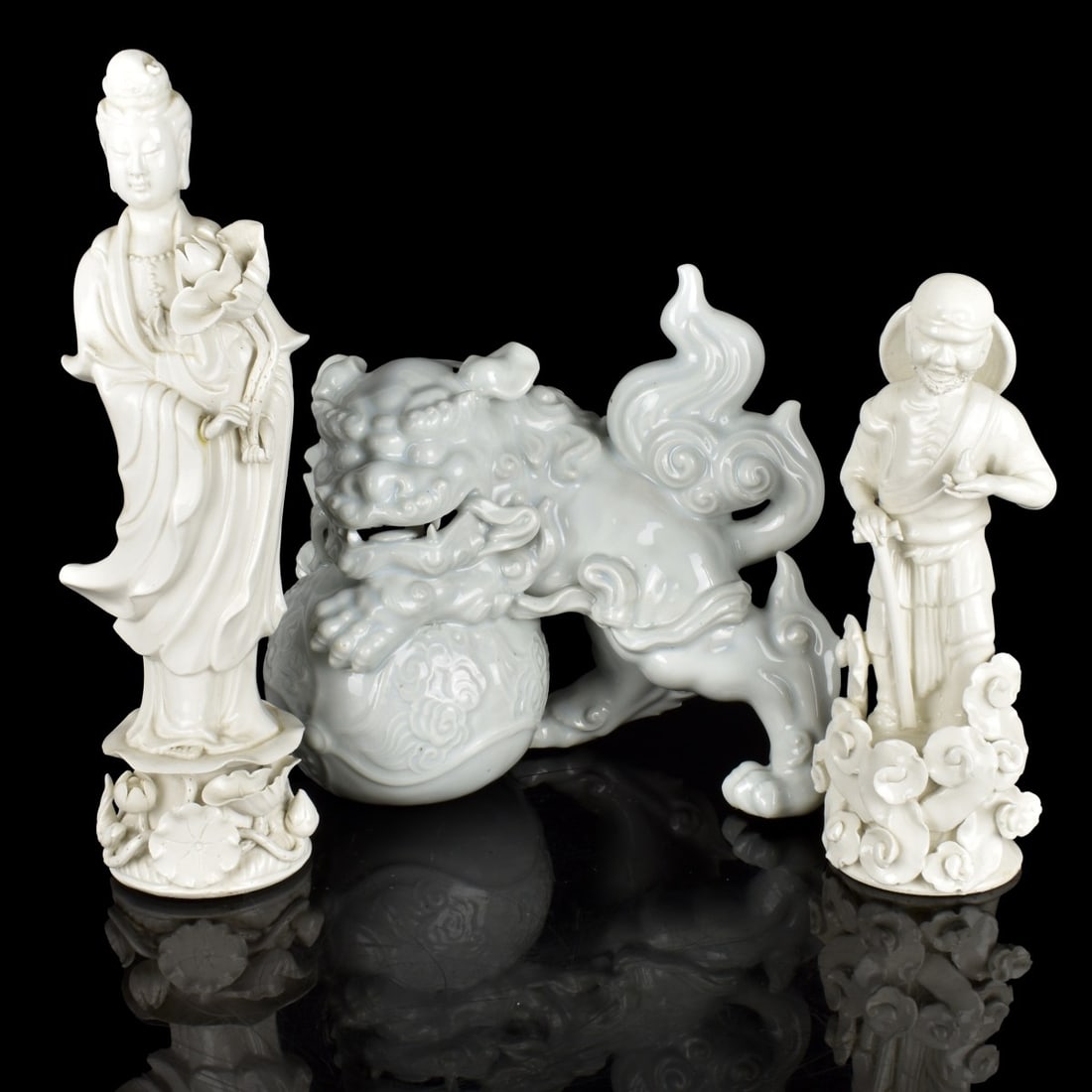 Chinese Blanc de Chine Figures: Three (3) Chinese Blanc de Chine Figurines. One (1) Guanyin figure standing holding a large flower with flowers to the base. Marked to the bottom. Measures: 11-3/4" H, 4" W, 3" D. One (1) Standing ric