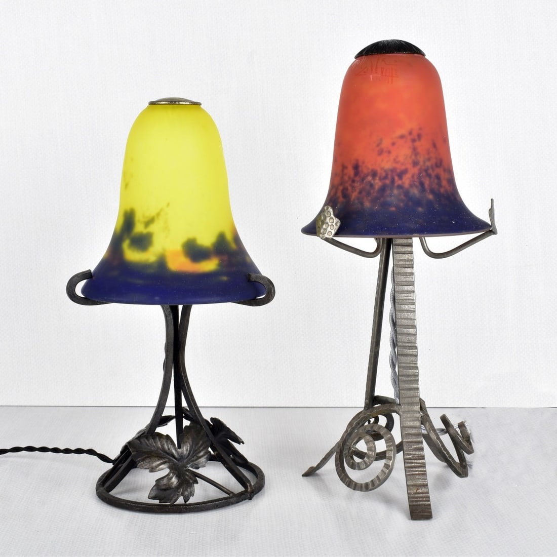 French Muller Fres Boudoir Lamps: Two (2) French Muller Fres Boudoir Lamps. Both with an art glass bell-shape shade, one is orange and mottled blue around the rim, the other is yellow and mottled blue and orange around the rim, signed