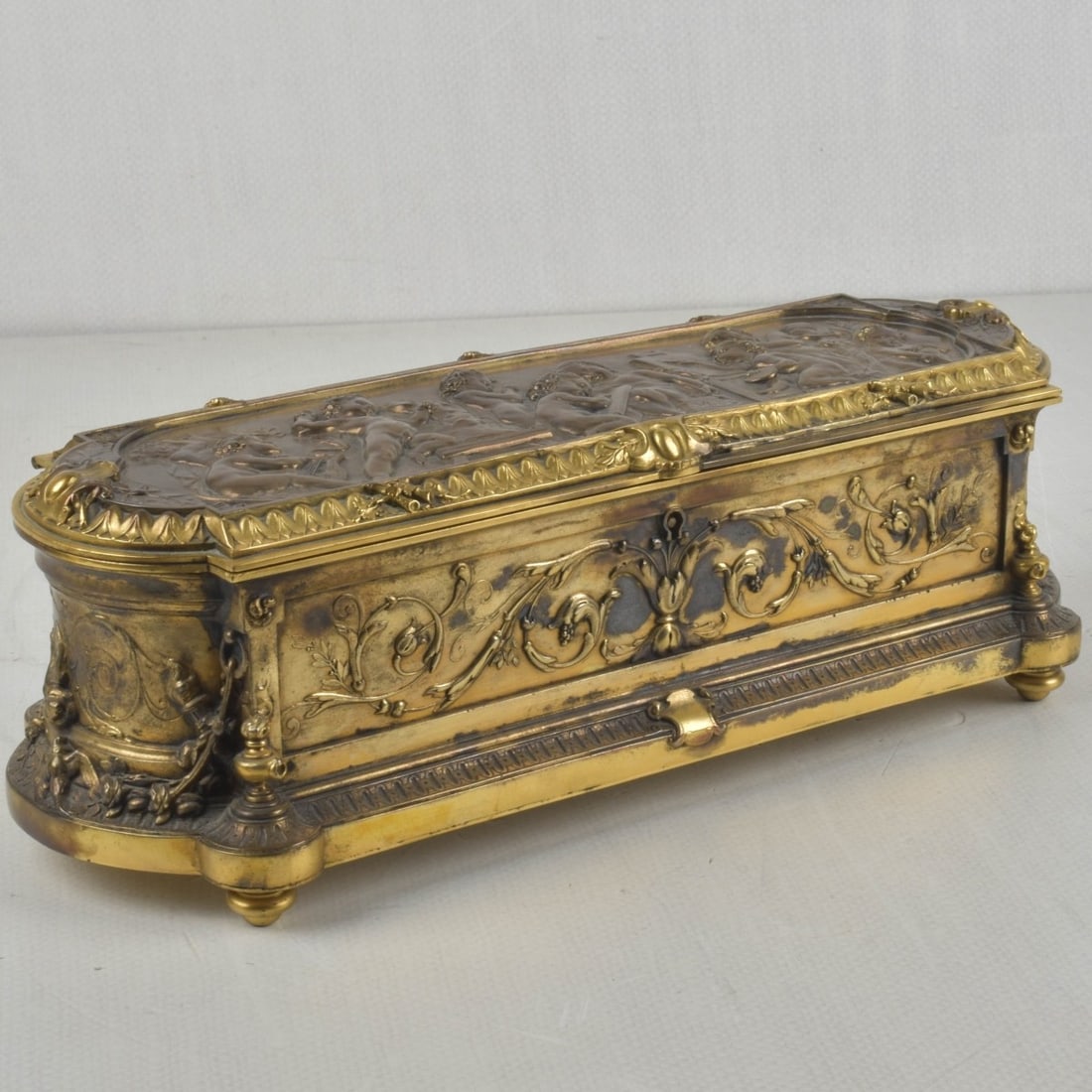 19th/20th Century French Gilt Bronze Box: 19th/20th Century French Heavy and Fine Gilt Bronze Jewel Boudoir Hinged Box with Repose Cherubs Depicting Them Painting, Sculpturing and Playing Music with Floral Scrolls with a Red Velvet Interior. 