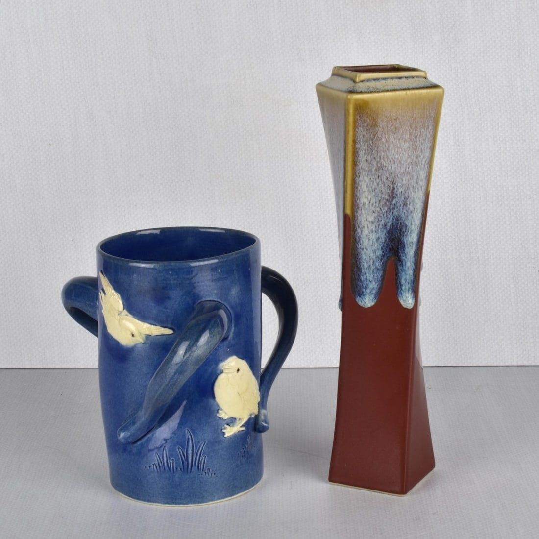 Japanese Pottery Vessels: Two (2) Japanese Pottery Vessels. Consisting of one (1) tyg three handled cup decorated with raised white flowers and incised leaves on a deep blue ground, artist mark to the bottom. Measures: 6" H, 3