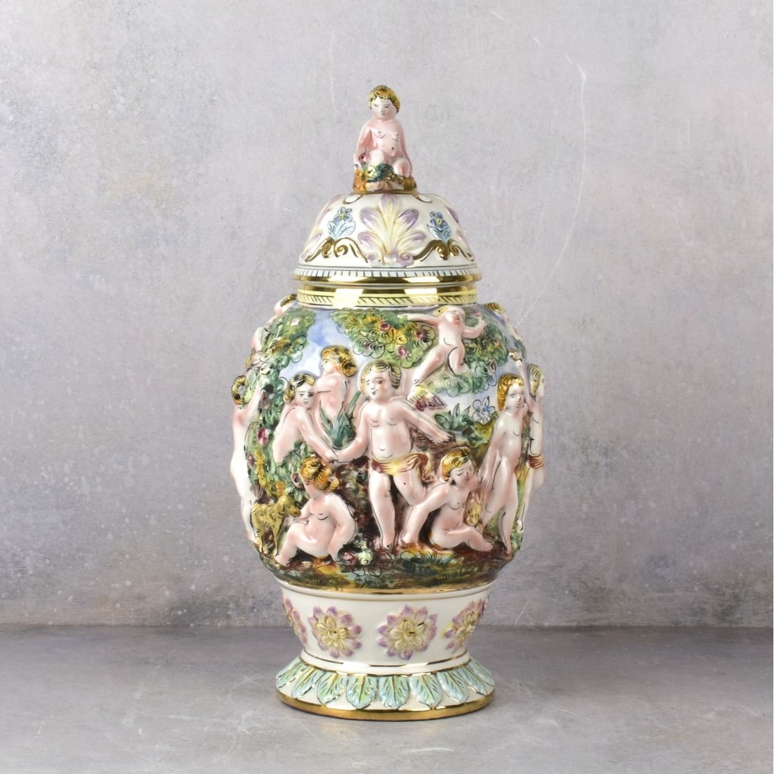 Vintage Italian Capodimonte Porcelain Covered Urn: Vintage Italian Capodimonte Porcelain Hand Painted Covered Urn. Decorated with putti and flowers all around with gold gilt enamel. Measures:17-3/4" H, 10" Dia. Kodner Galleries offers phone and absent