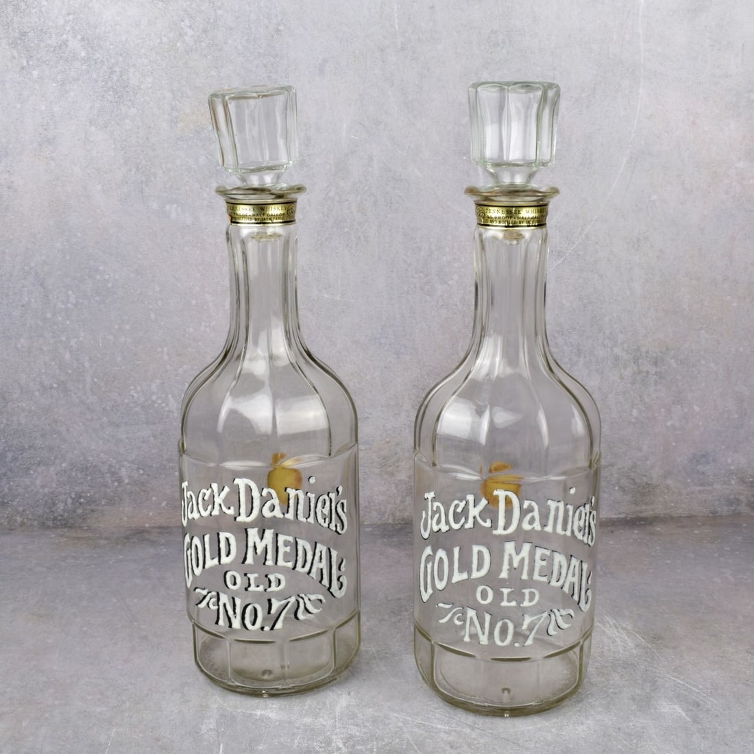 Vintage Jack Daniels Gold Medal Bottles: Two (2) Vintage Jack Daniels Gold Medal Old No. 7 Bottle with Stoppers. Measures: 15-1/2" H, 4-1/2" Dia. Kodner Galleries offers phone and absentee bidding at a low, flat 21% buyer?s premium without s