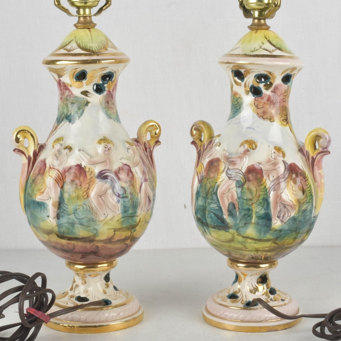 Pair of Italian Capodimonte Lamps: Pair of Italian Capodimonte Table Lamps. Circa 1980's. Decorated with hand-painted floral designs and high relief cherub figures and gilded details. Porcelain body of lamps measure:13" high, 6-1/2" wi